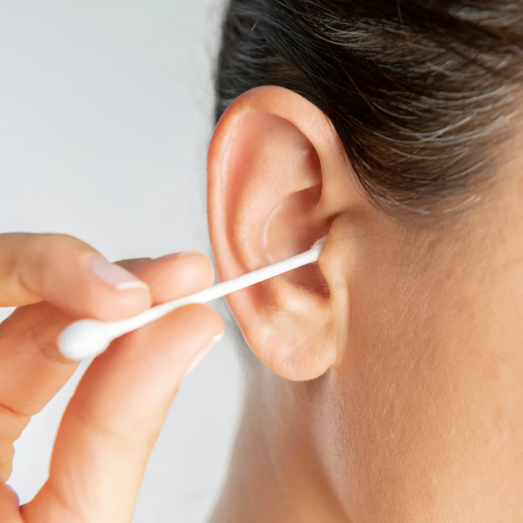 A person cleaning their ear with a cotton swab, holding it near the ear canal.