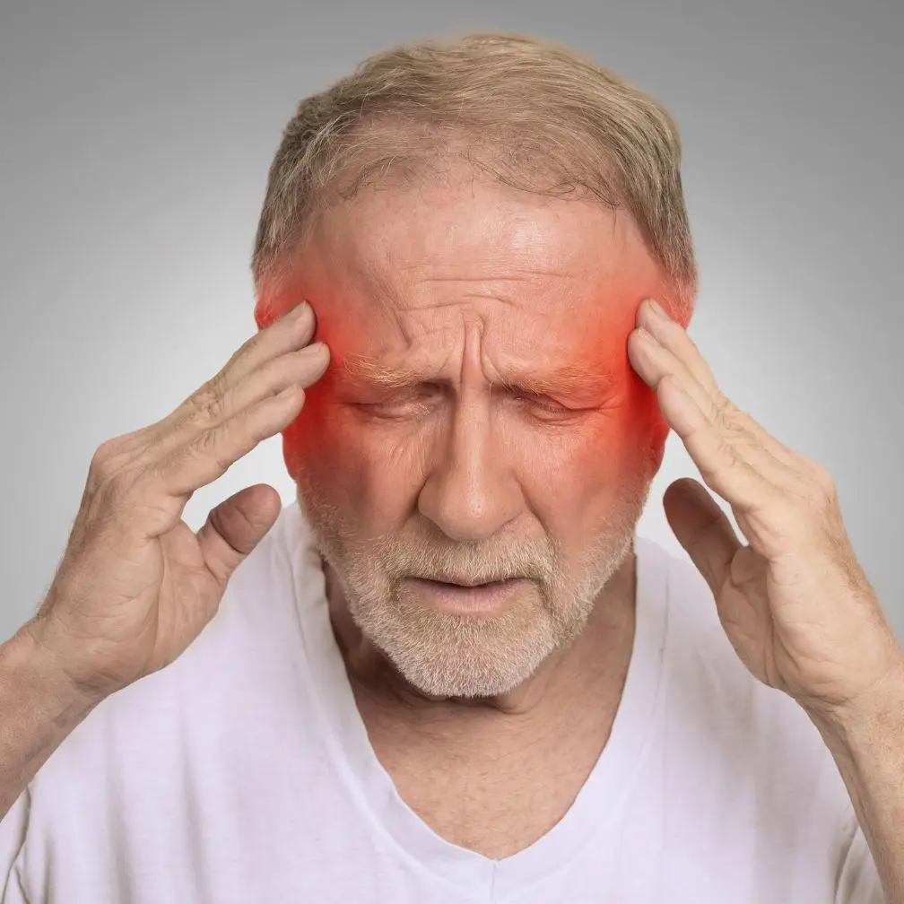 Older man with closed eyes holds his temples in pain, red highlights on both sides of his head indicate a headache or migraine.