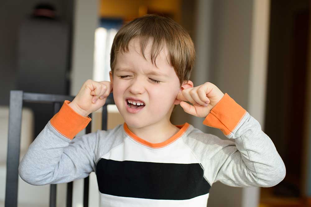 Boy pressing his fingers into both ears as if they feel clogged, a symptom McLean Hearing Center evaluates in Dallas, TX
